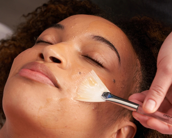 A hand brushes a facial treatment serum onto the face of a woman with her eyes closed